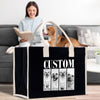 A woman is sitting on a couch, reading a book, while a dog is in the background. A black tote bag with a white handle and the word "CUSTOM" printed on it is placed in front of the couch.