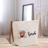A white tote bag with a printed design of a cow's head and floral elements, along with the name "Sarah" written on it.