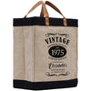 A beige tote bag with a black trim and leather handles, featuring a vintage-style design with text and graphics.