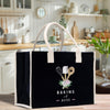 A black tote bag with a white handle and a design featuring baking utensils and flowers, placed on a kitchen counter.