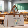 A beige canvas tote bag with the text "Mrs. Parker's Teacher Stuff" printed on it, placed on a wooden surface.