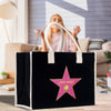 A black tote bag with a pink star-shaped logo on it, placed on a wooden surface.
