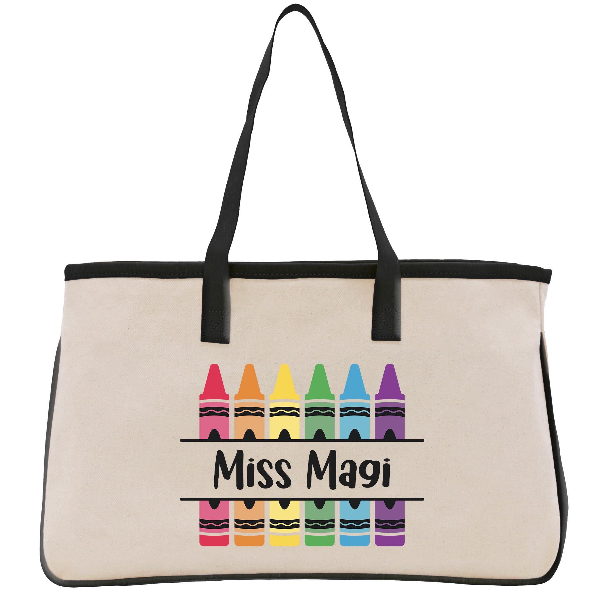A beige canvas tote bag with a black handle and straps, featuring a colorful design of crayons arranged in a row and the text &quot;Miss Magi&quot; printed on it.