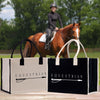 two large bags with the word "Equestrian" printed on them, placed on a wooden surface. In the background, there is a person riding a horse.