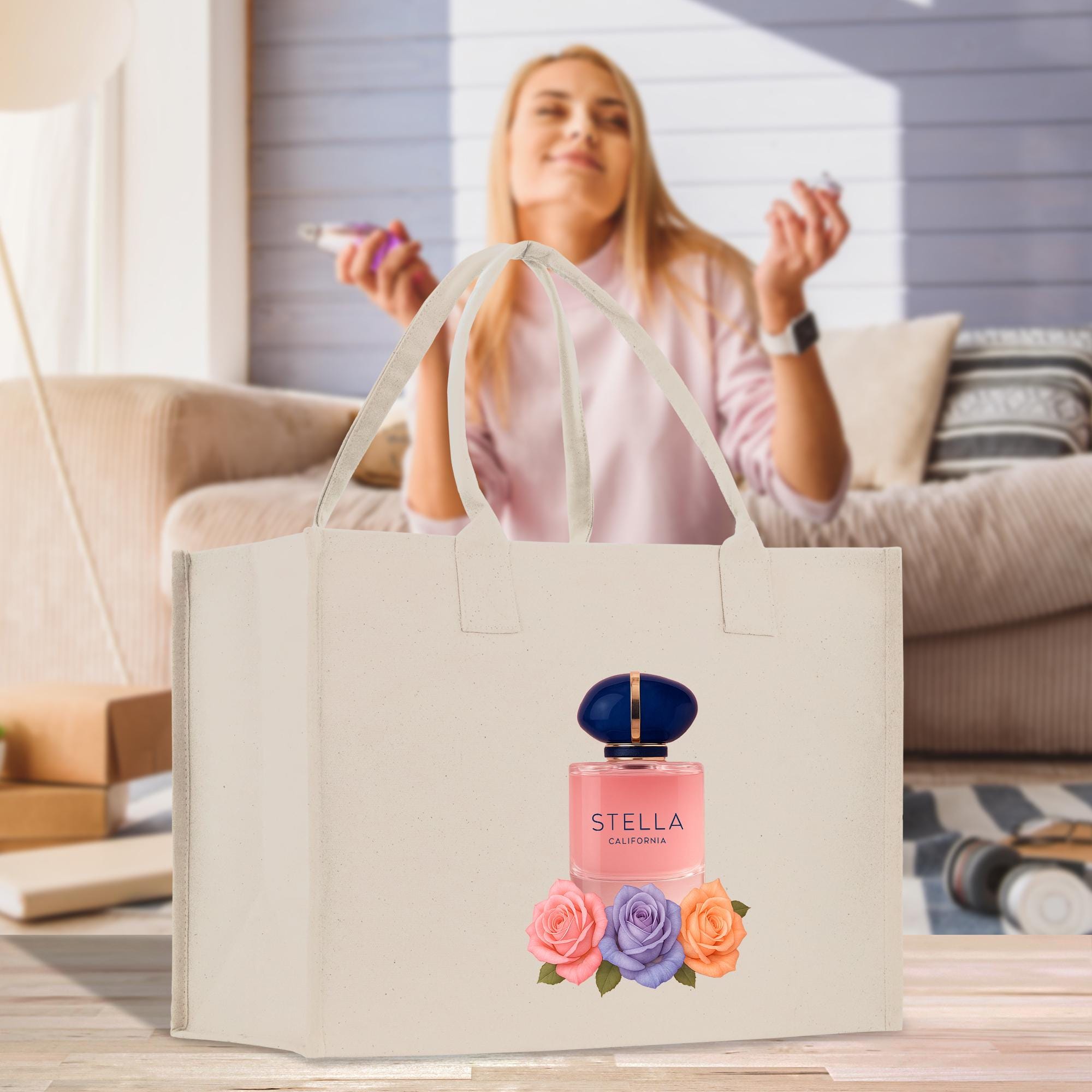 A woman is sitting on a couch in a living room, holding a phone and smiling. A large beige tote bag with a perfume bottle image and flowers is placed in front of her.