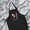 A black apron with a pink floral design and the text "MONICA GREEN" printed on it, placed on a marble surface.