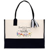 A beige tote bag with a black handle and a black and white striped ribbon tied around it. The bag has a floral design on the front and text printed on it.