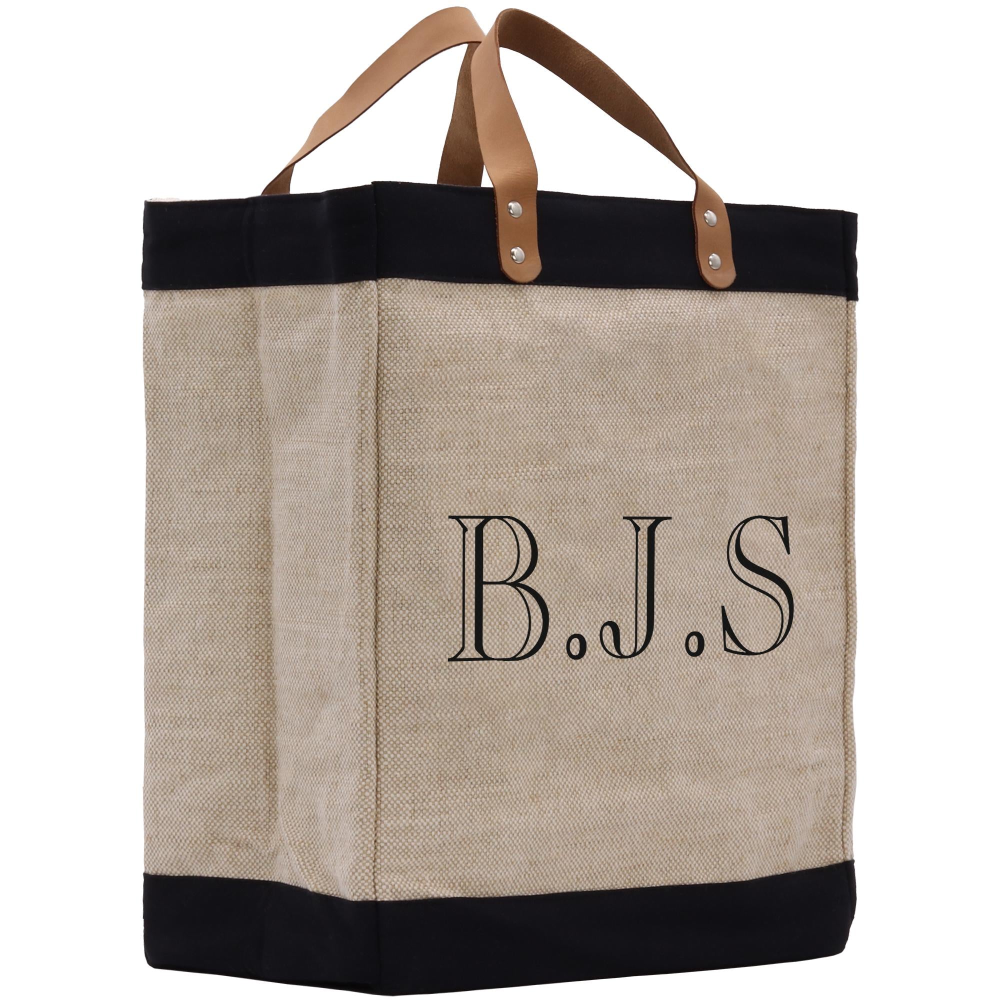 A beige tote bag with black trim and leather handles, featuring the initials &quot;B.J.S.&quot; printed on it.