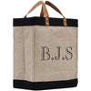 A beige tote bag with black trim and leather handles, featuring the initials "B.J.S." printed on it.
