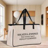A large canvas tote bag with the text "WALKER & JENNINGS Real Estate Agent ASHLEY EDWARDS" printed on it, placed on a wooden floor in a room with a window and a wooden chair.