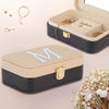 a beige and black jewelry box with a gold lock, containing various pieces of jewelry such as necklaces and earrings. The box is placed on a pink background, and there is a bouquet of white flowers in the foreground.
