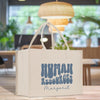 A white tote bag with the text "HUMAN RESOURCES Margaret" printed on it, placed on a wooden surface in a room with a window and plants in the background.