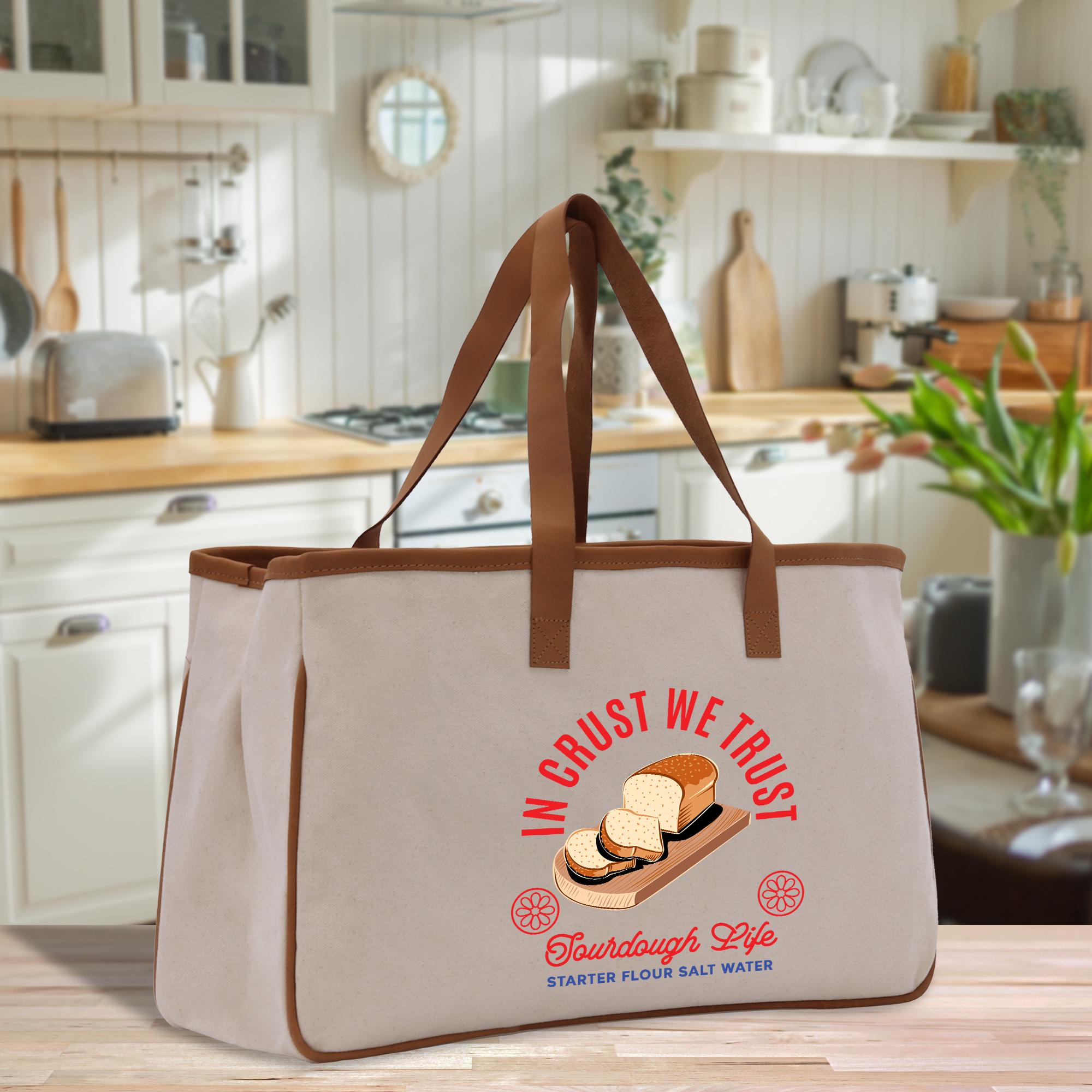 A beige tote bag with a graphic design of bread and the text &quot;In the trust&quot; printed on it, placed on a kitchen counter.