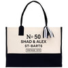 A beige tote bag with black trim and a black ribbon tied around the handle. The bag has text printed on it, which reads "No 50 SHAD & ALEX ST-BARTS VINTAGE 1975".
