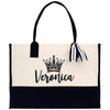 A beige tote bag with a black handle and a black and white striped ribbon tied around it. The bag has a crown design on the front and the name "Veronica" printed on it.