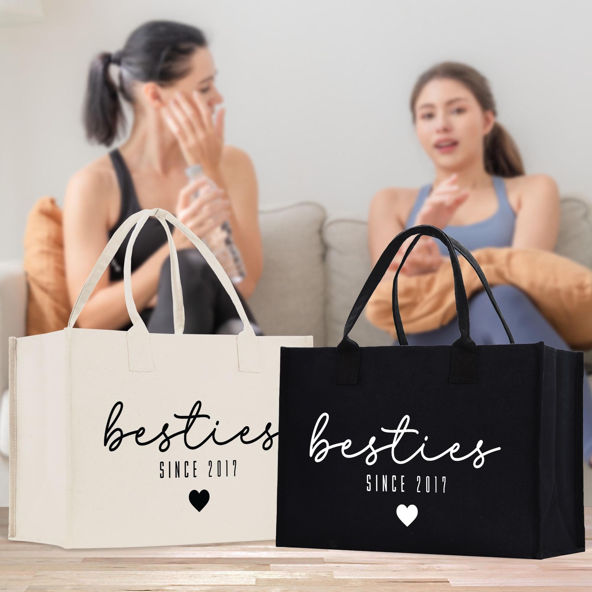 Two women sitting on a couch, one holding a water bottle, with two bags labeled &quot;besties since 2017&quot; in front of them.