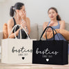 Two women sitting on a couch, one holding a water bottle, with two bags labeled "besties since 2017" in front of them.