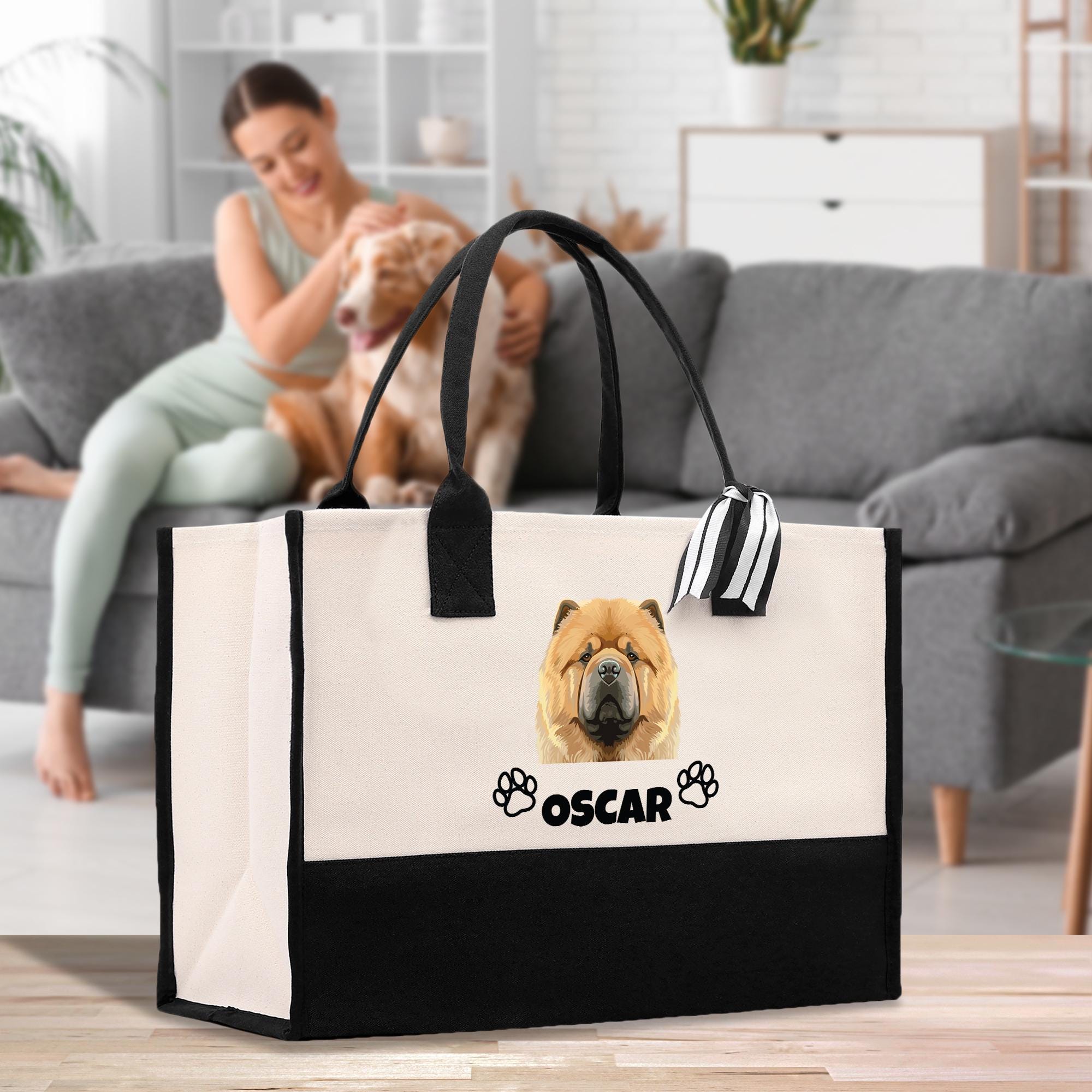 A woman is sitting on a couch in a living room, petting a dog. A large tote bag with a dog image and the name &quot;OSCAR&quot; printed on it is placed on the floor in front of the couch.