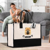 A woman is sitting on a couch in a living room, petting a dog. A large tote bag with a dog image and the name "OSCAR" printed on it is placed on the floor in front of the couch.
