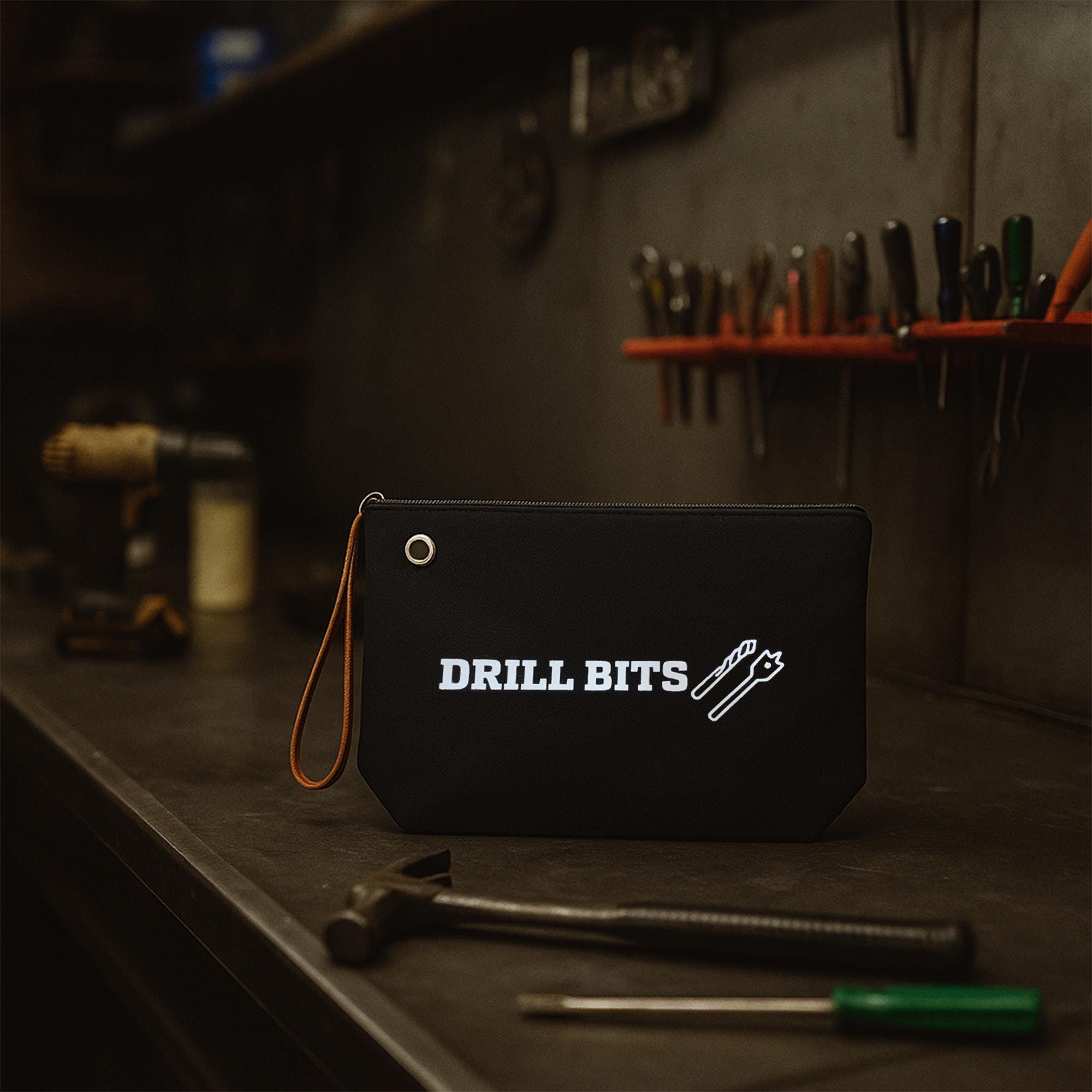 A black tool bag with the text &quot;DRILL BITS&quot; printed on it, sitting on a workbench with various tools and equipment in the background.