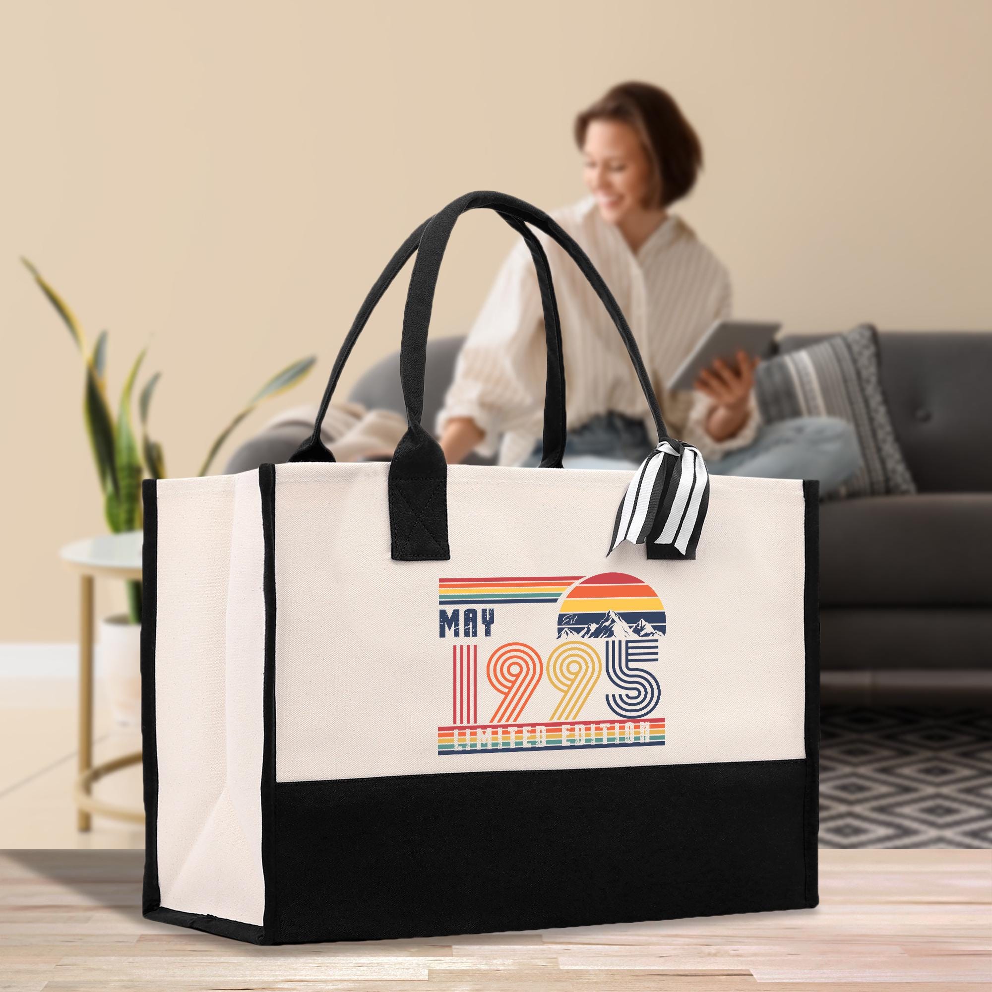 A large white tote bag with a colorful graphic and text printed on it, placed on a wooden floor in a living room setting.