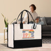 A large white tote bag with a colorful graphic and text printed on it, placed on a wooden floor in a living room setting.