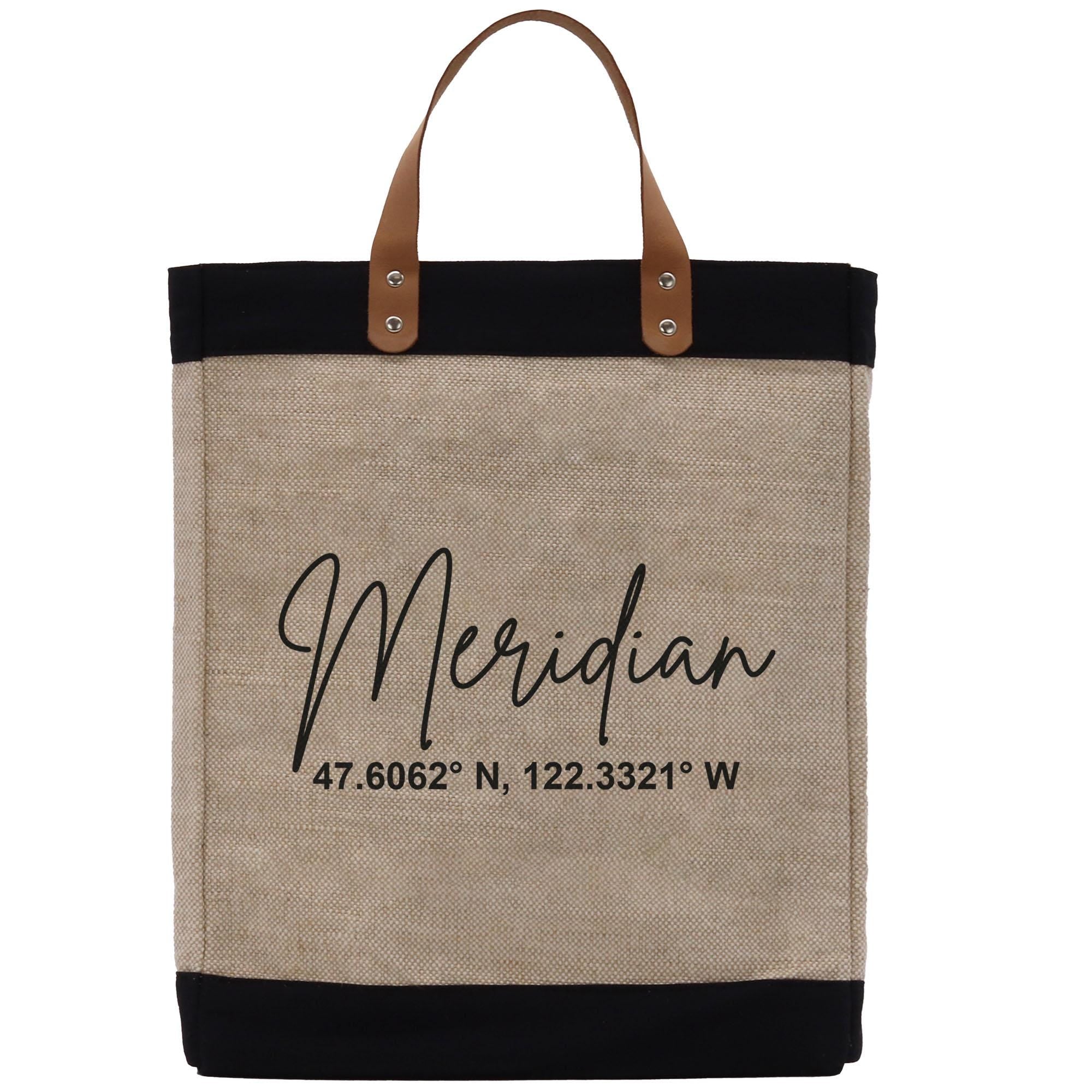 A beige tote bag with black trim and leather handles, featuring a personalized text that reads &quot;Meridian 47.6062° N, 122.3321° W&quot;.