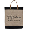 A beige tote bag with black trim and leather handles, featuring a personalized text that reads "Meridian 47.6062° N, 122.3321° W".