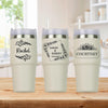Three personalized tumblers with names and dates printed on them, placed on a wooden surface.