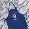 A blue apron with a white letter "B" and a Santa hat on it, placed on a marble surface.