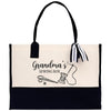 A tote bag with a black and white design featuring sewing-related items such as scissors and a spool of thread, along with the text "Grandma's Sewing Box".