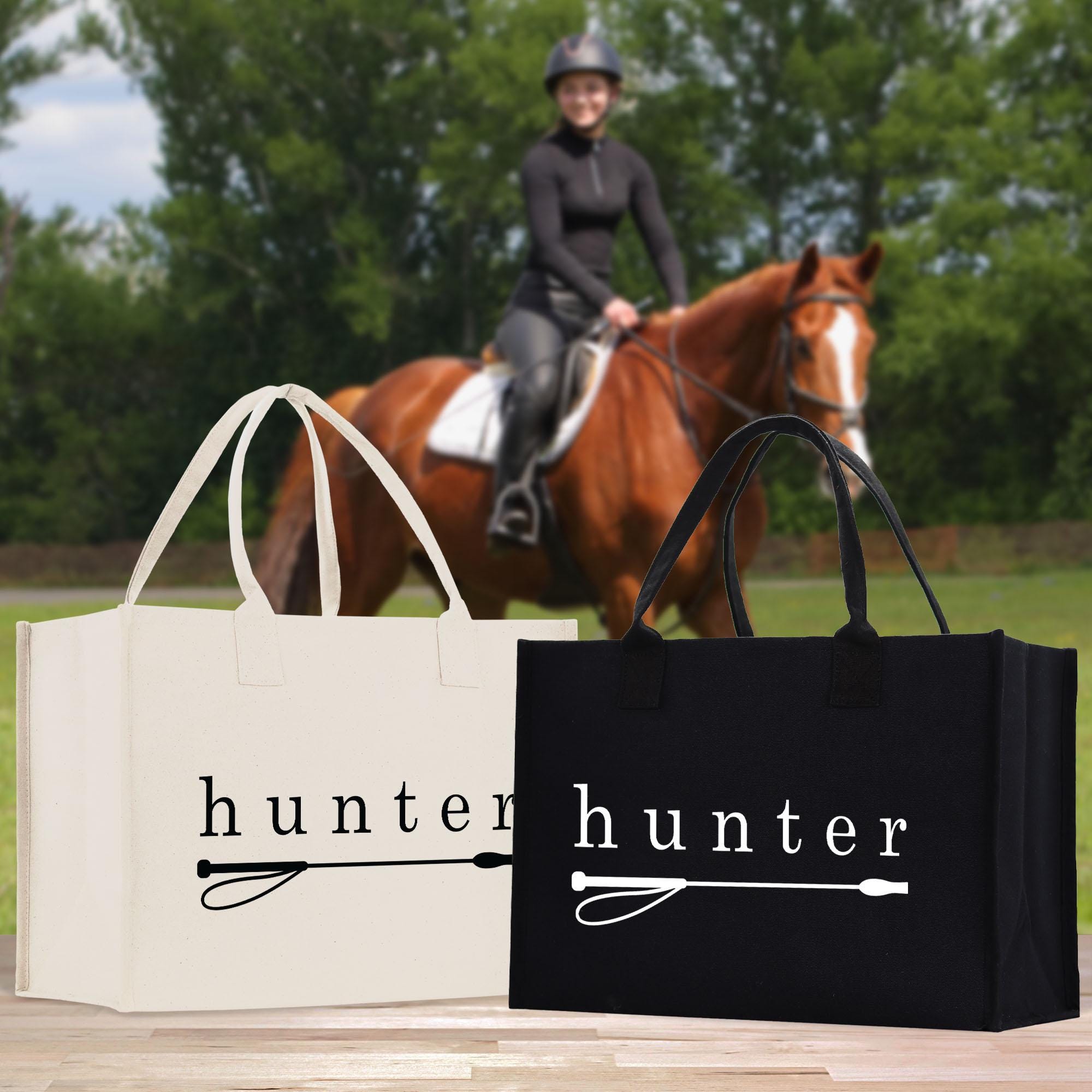 A person riding a horse in a field, with two bags labeled &quot;Hunter&quot; in the foreground.