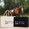 A person riding a horse in a field, with two bags labeled "Hunter" in the foreground.