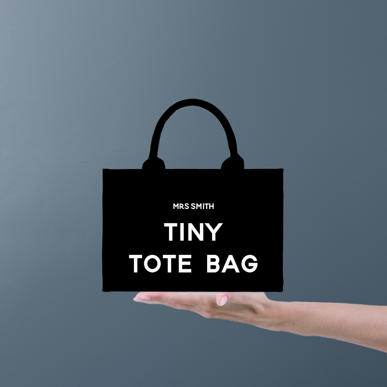 a hand holding a black bag that says tiny tote bag