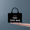 a hand holding a black bag that says tiny tote bag